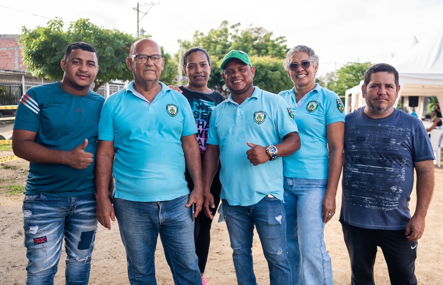 Grupo de seis personas, algunas con camisas celestes con insignias, posando juntas al aire libre, ayudando en la recoleccion de basura.