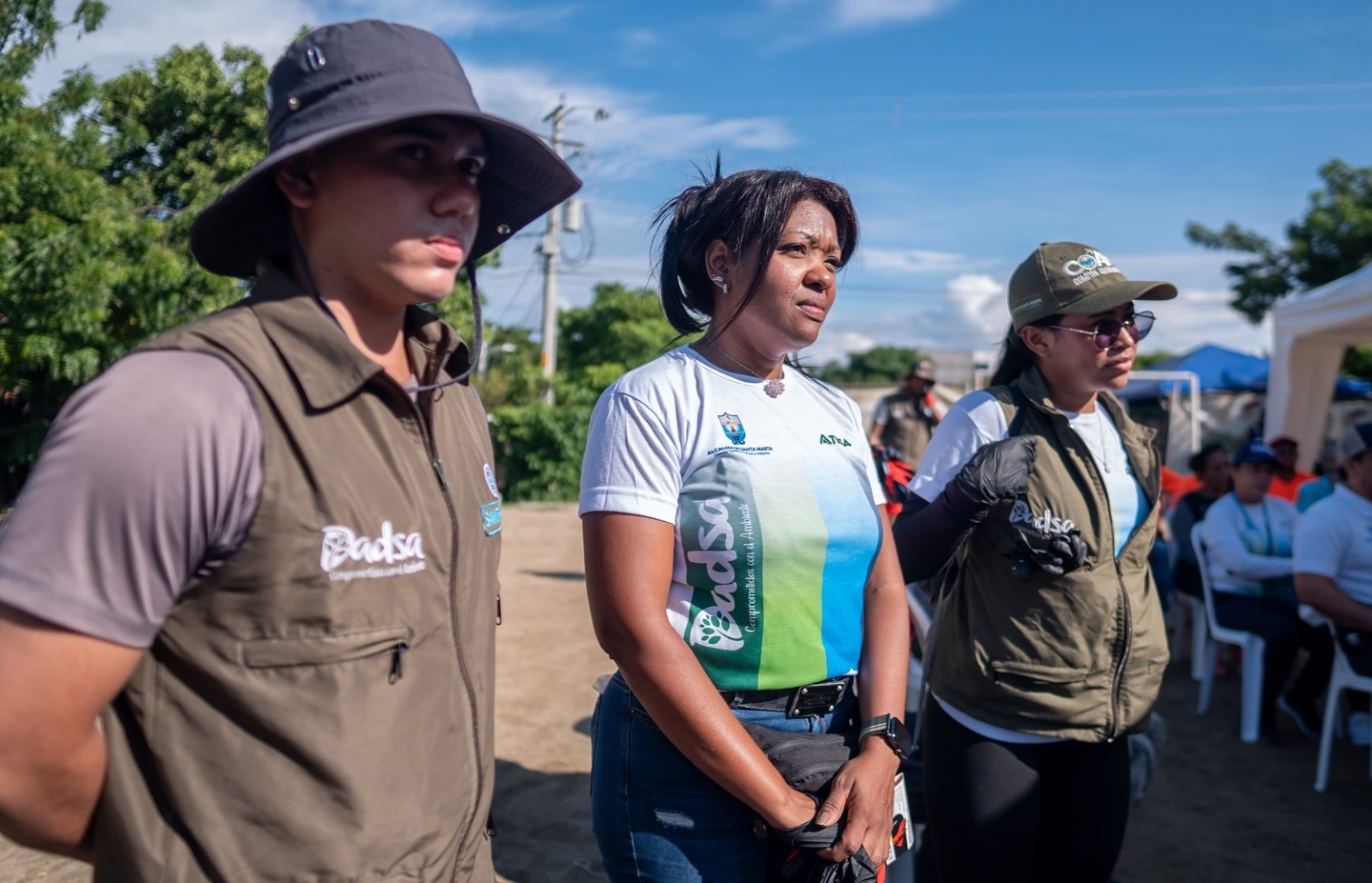 res personas con uniformes y chalecos del DADSA organizaciones ambientales, observando atentamente en una jornada comunitaria al aire libre.