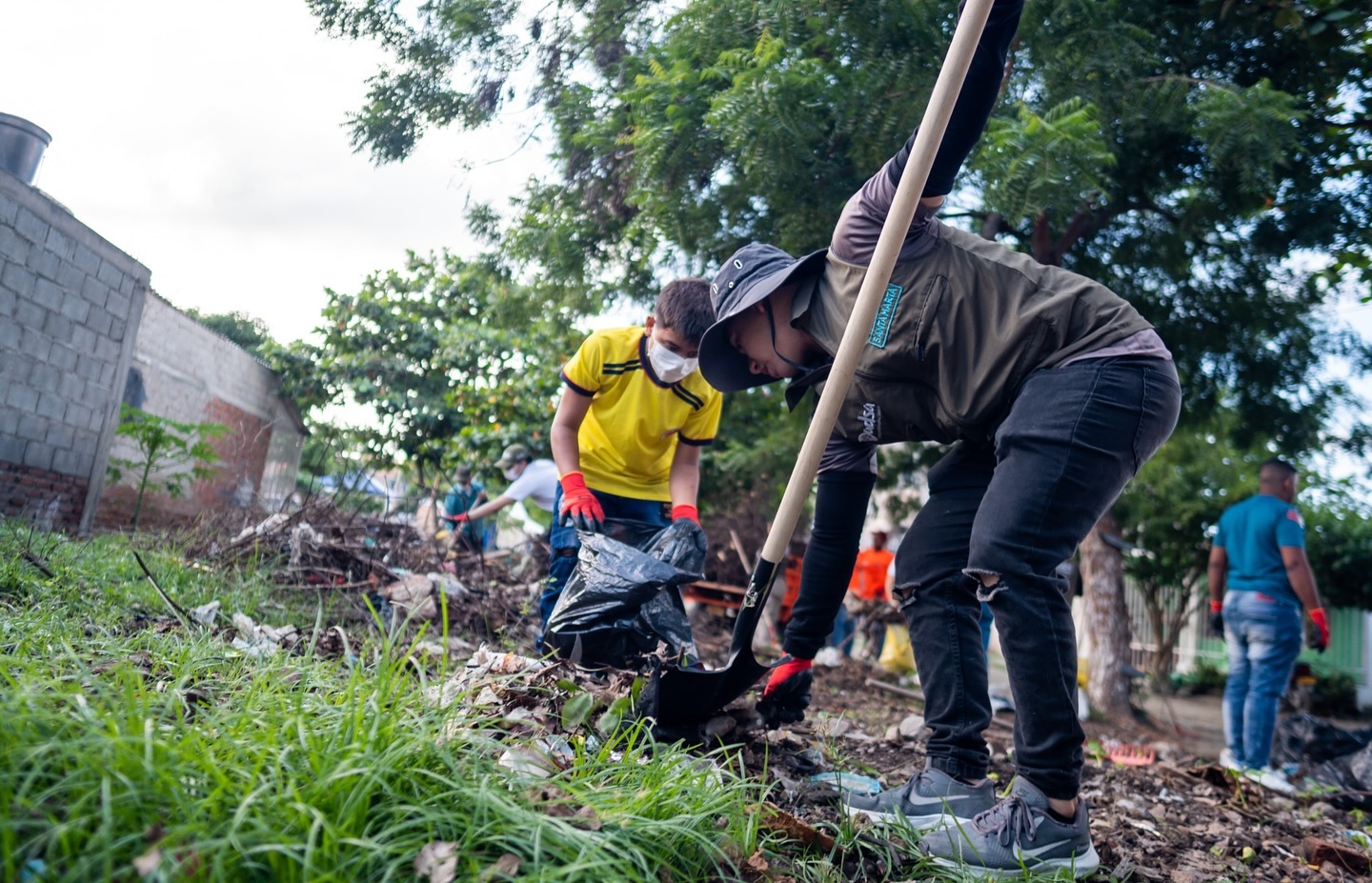 Personas trabajando juntas para limpiar una zona verde, utilizando bolsas y palas para recoger desechos.